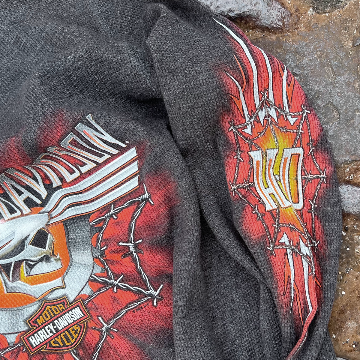 Faded black Harley-Davidson flame and barbed-wire graphic shirt on stone