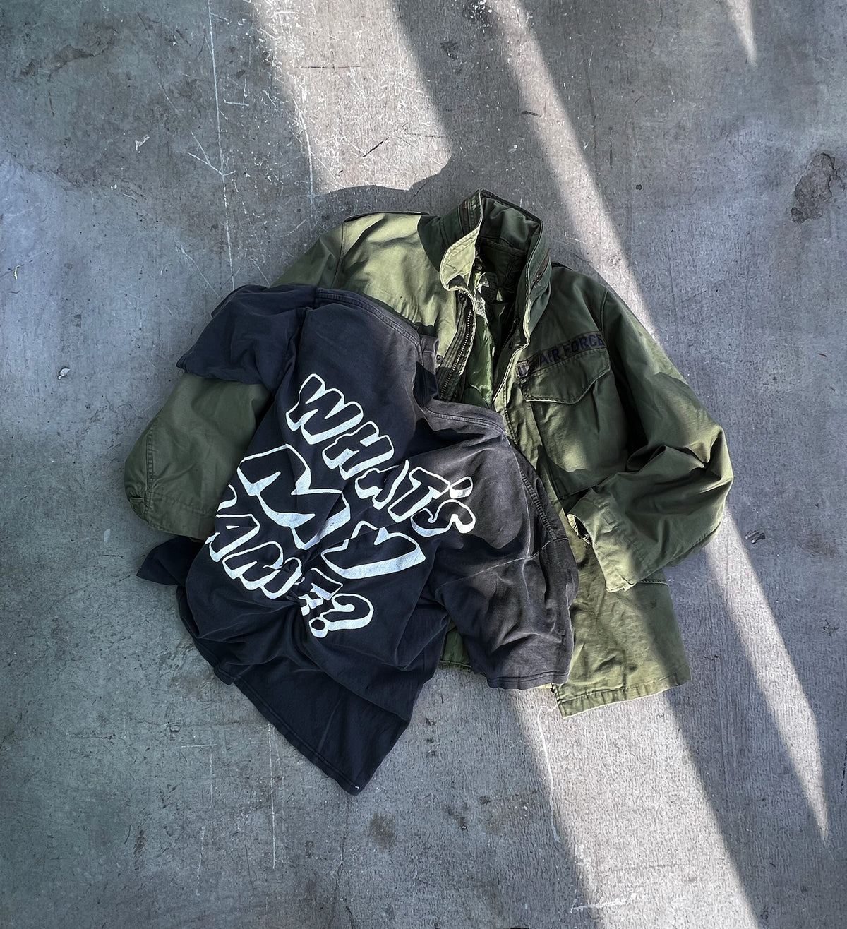 Vintage U.S. Air Force field jacket layered with a black graphic T-shirt on concrete.