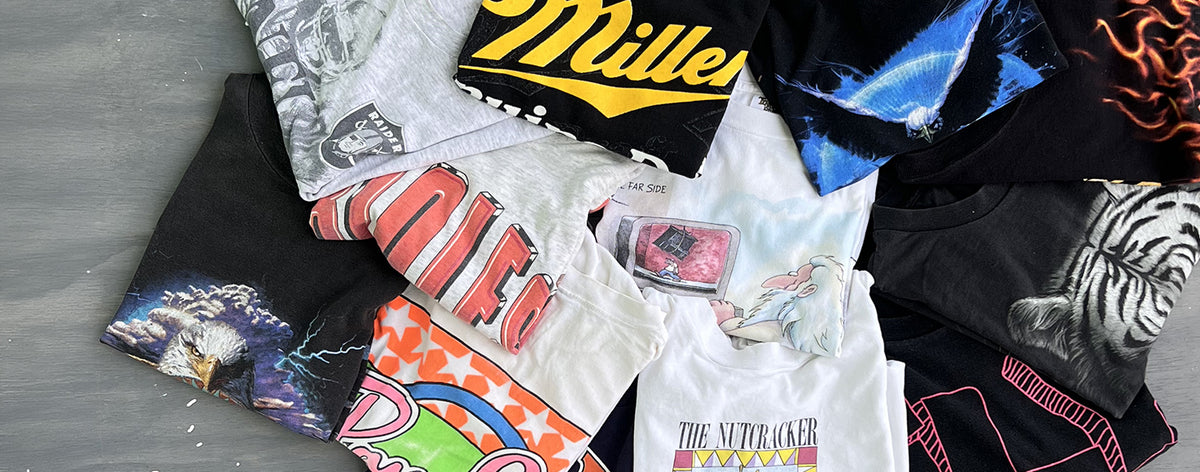 Assorted vintage graphic T-shirts arranged on a gray wood floor for the Oasis of Relics Relic Runs collection.